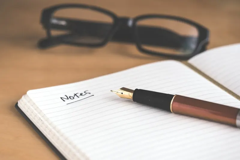 Notebook, fountain pen and glasses on a warm wooden desk