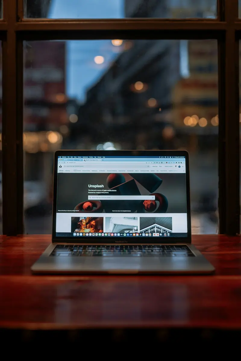 Laptop on a wooden desk beside a window in warm evening light